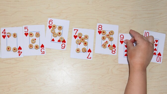 A child places Cheerios on cards from a deck, corresponding with their number.