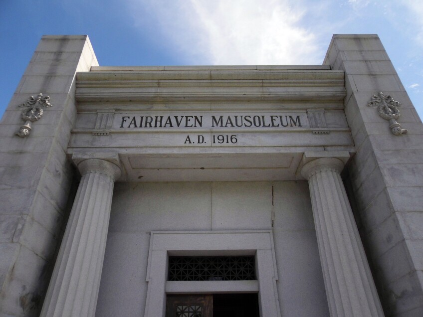 A white marble mausoleum with two columns on either side of the entrance. Across the top of the entrance, engraved into the stone, reads "Fairhaven Mausoleum A.D. 1916."