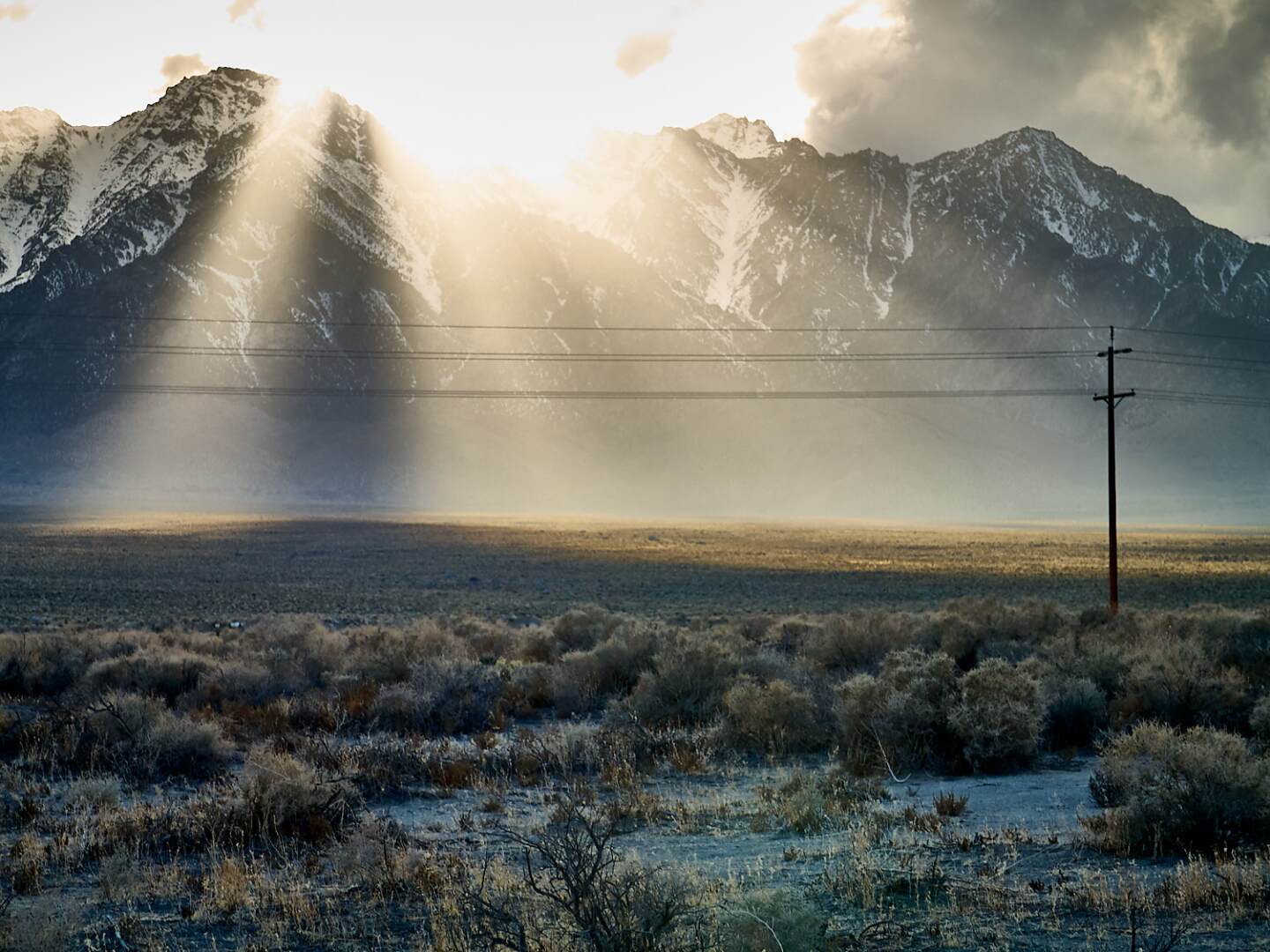 A photograph of rays of sunlight shining through mountain peaks in the Sierra Nevada desert.