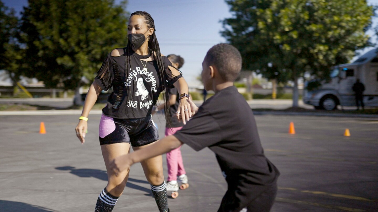 A young woman and a boy roller skate.