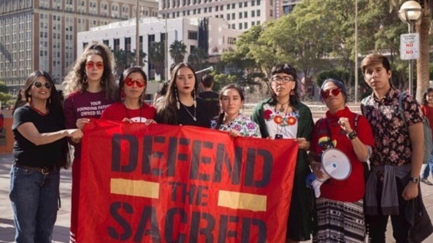 The fourth person from the left, Bii Gallardo help hold a banner that reads "DEFEND THE SACRED" during the L.A. Women’s March in January 2020.