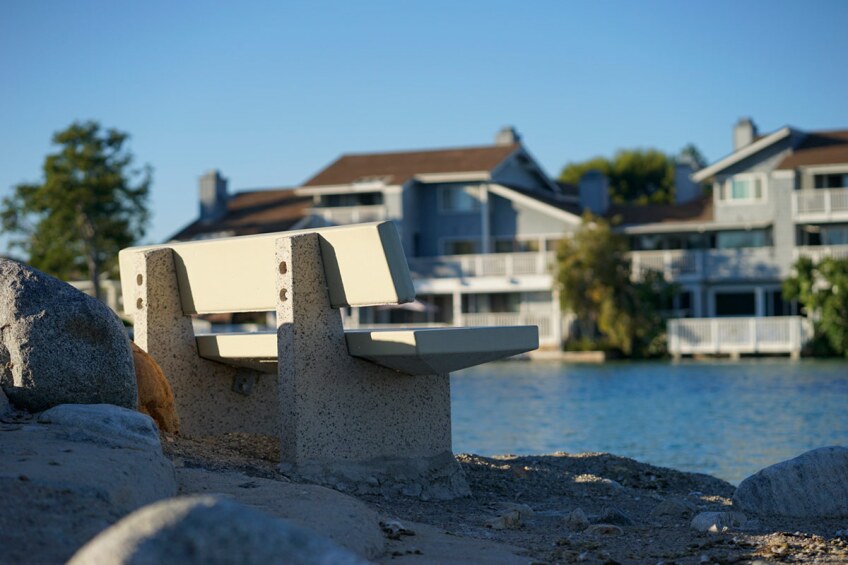 A cement bench faces a body of water and waterfront homes. 