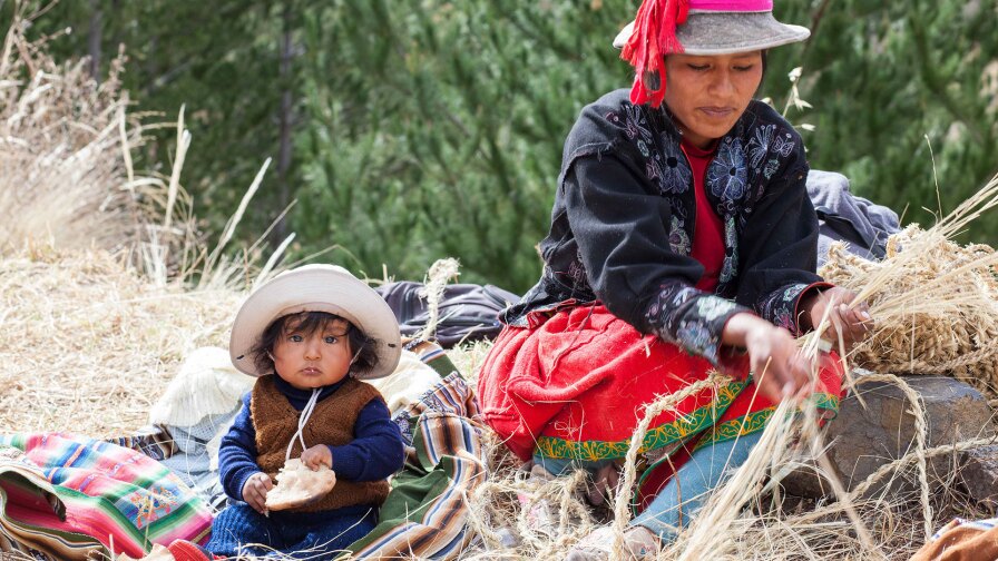 A baby plays alongside a woman braiding rope for the Q'eswachaka Bridge reconstruction.