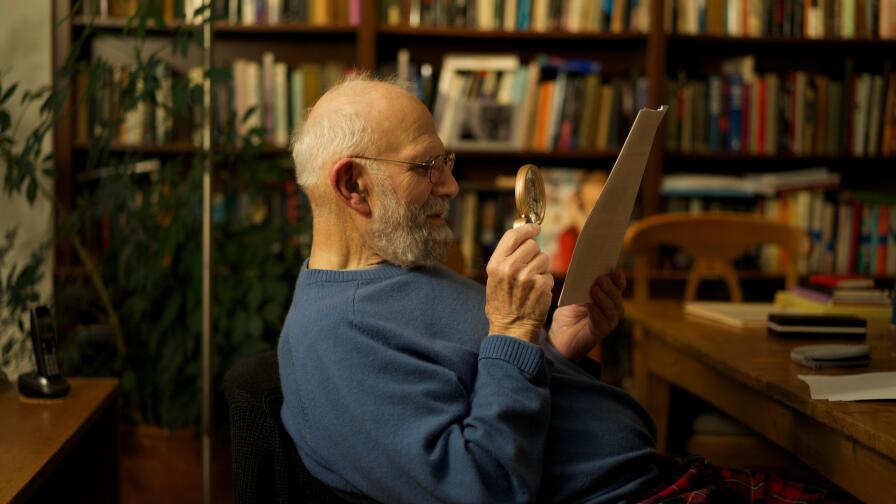 Oliver Sacks examines a document in his hand with a magnifying glass.