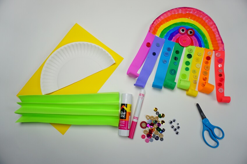 a craft made out of a paper plate made to look like an octopus decorated with colorful construction paper strips as tentacles alongside construction paper sheets, glue, scissors and glitter