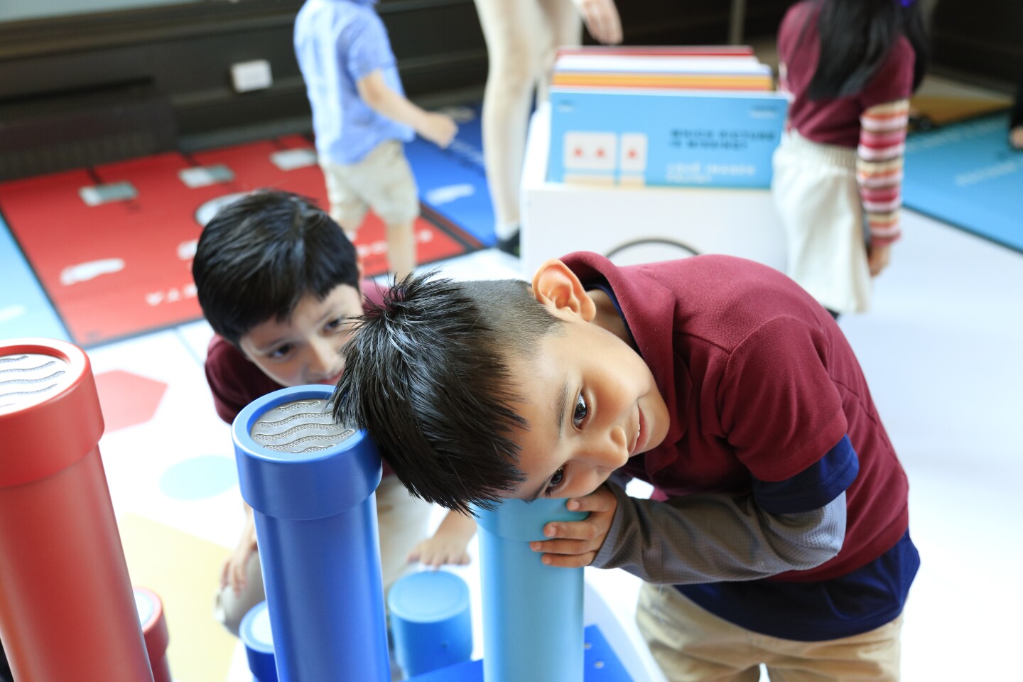 A small boy smiles as he places his ear over a colorful tube and listens.