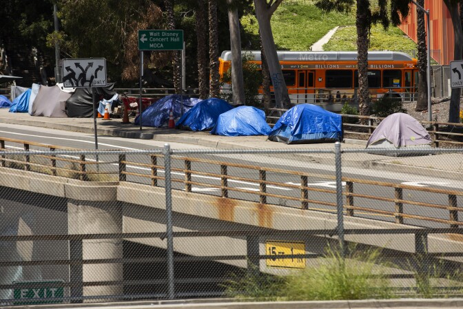 a row of tents on the sidewalk next to a Walt Disney Concert Hall directional sign