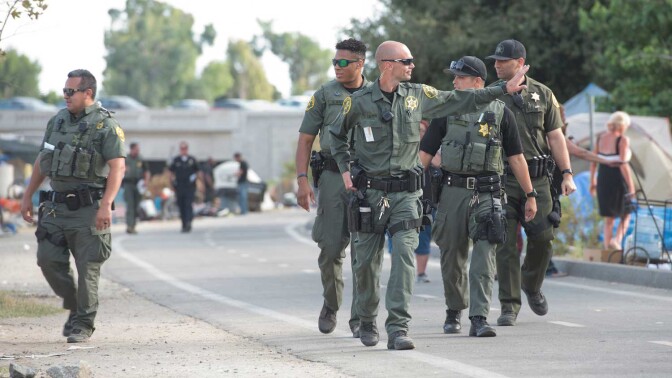 Orange County Sheriff's Deputies walk along Santa Ana Riverbed homeless camp