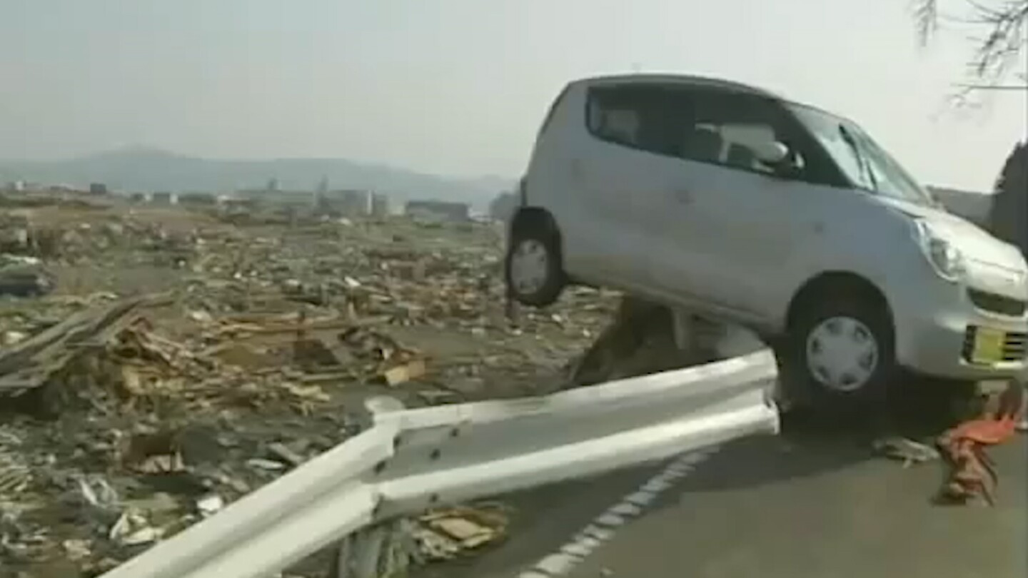 A car barely hangs over a railing in the aftermath of the 2011 Tohoku earthquake in Japan.