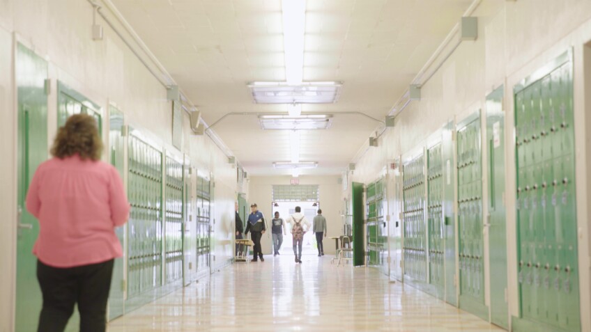 Teacher Walks Down a School Hallway