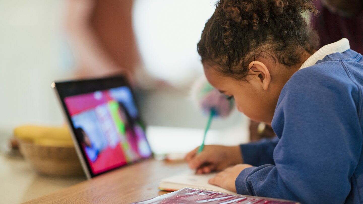 A close-up shot of a schoolgirl doing homework with the help of a digital tablet. She is at home sitting at the kitchen table.