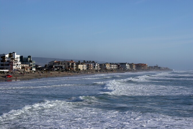 Houses nested along the imperial beach coast in the background while waves stir and crash in the foreground.