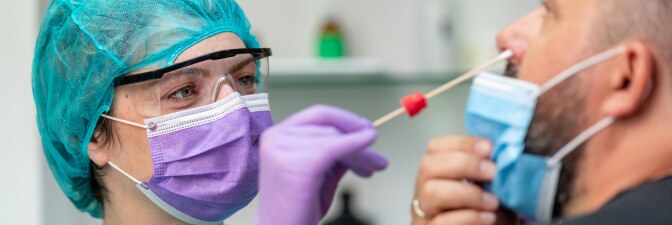 A female doctor in protective workwear does a nose swab COVID-19 test on middle aged man wearing a protective face mask. | iStock