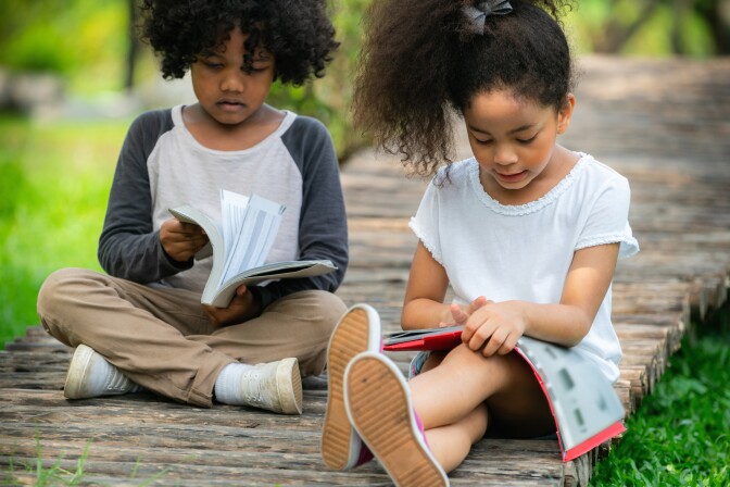 A little girl and boy read outside.