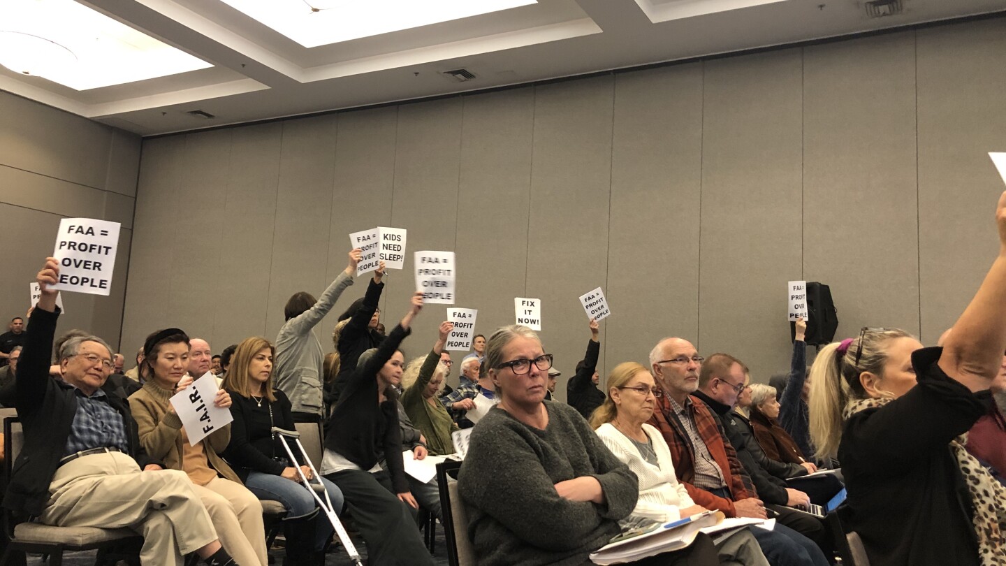 People holding signs against F.A.A while sitting in a meeting about Burbank Airport Noise