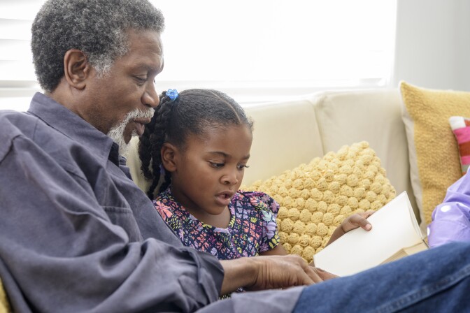 African American grandfather listening to girl read book