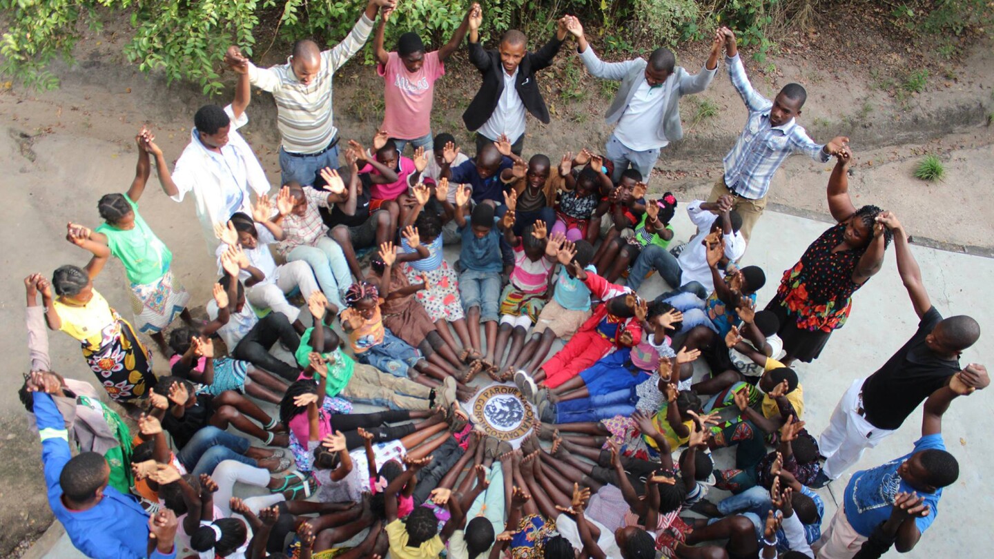 A group of many people join hands in a circle and raise their arms.