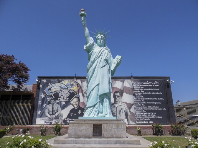 A replica of the statue of liberty stands tall in front of a mural featuring an American flag and photos of emergency services like firefighters and police officers.
