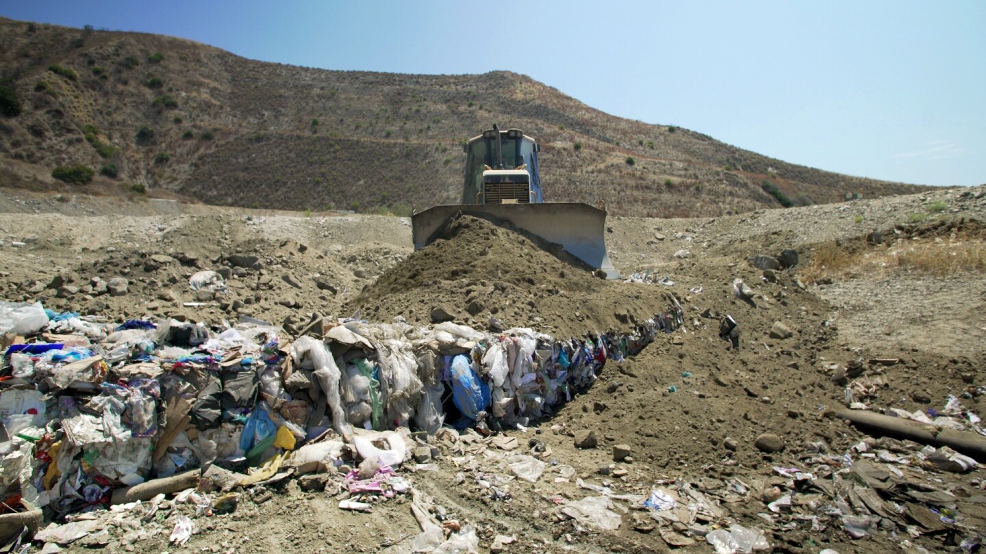 Dirt being pushed over trash by tractor in a landfill | Still from "Life in Plastic: California's Recycling Woes"