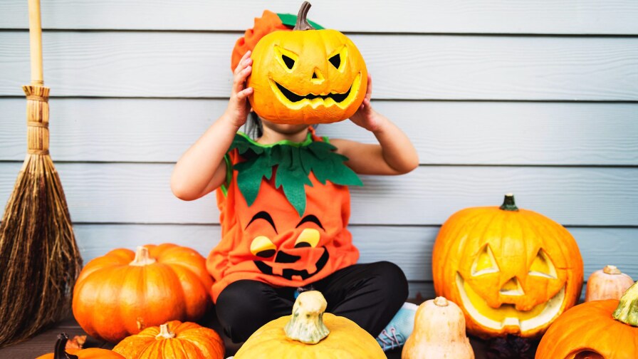 child dressed up as a jack o lantern holds a pumpkin