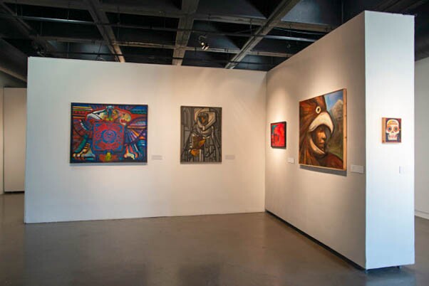 Two white art gallery walls form an L-shape. On the walls are five pieces of framed artwork, all paintings.