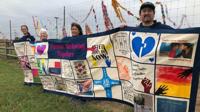 Four people hold a colorful quilt in protest