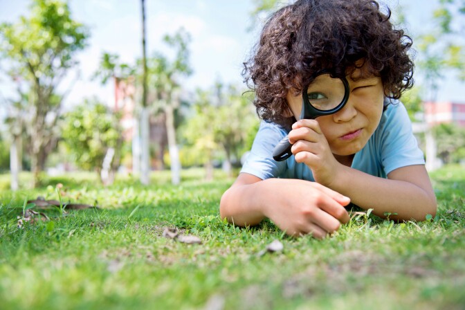 Little boy with magnifying glass in park outside community science citizen science neighborhood sicence
