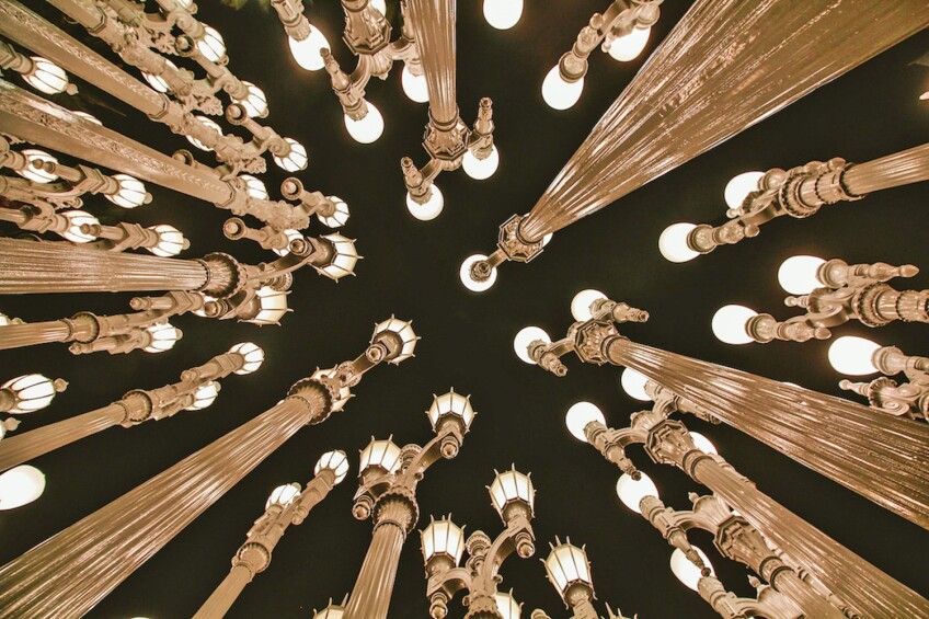 A photo of various street lamps grouped together. The photo is shot upwards, from the foot of the lamp posts, with the lamps glowing against a dark night sky.