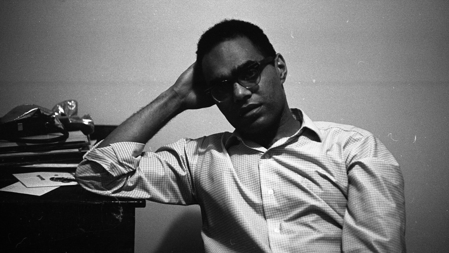 Portrait Of Robert Parris Moses in black and white. He is leaning his elbow against a table and holding his head in his hand.