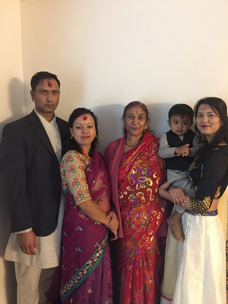 Three women, one holding a small child, in saris stand next to a man.